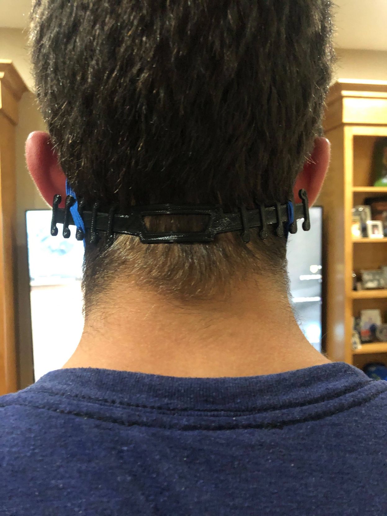 A man models a plastic product that attaches to the straps of a face mask and wraps around the head to take the pressure off ears